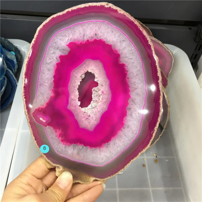Geode slice with pink interior held by a hand on a tiled floor.
