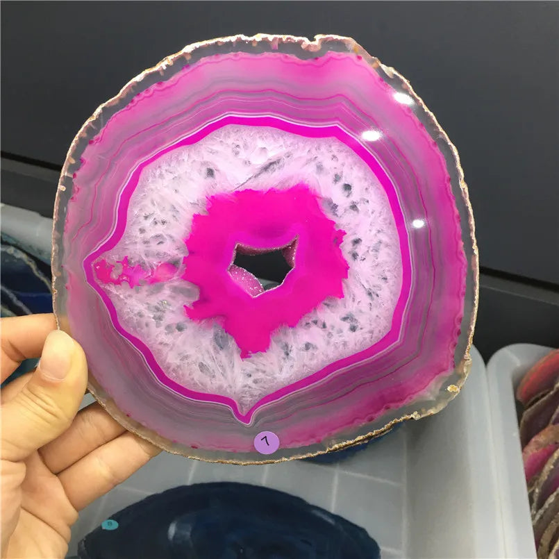 Close-up of a pink and white agate slice held by a hand against a dark background.