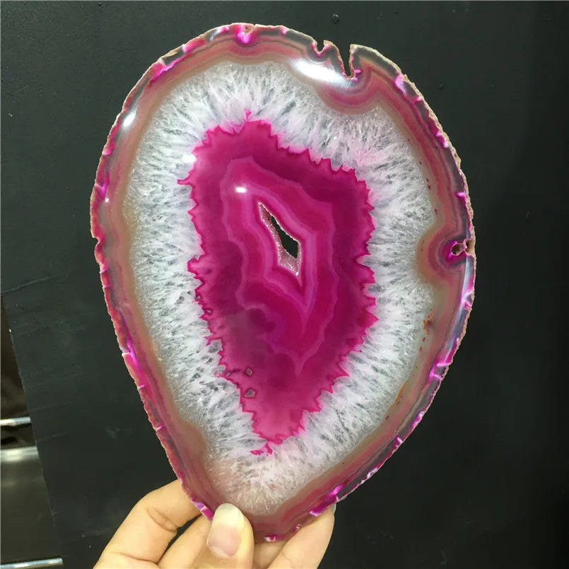 Geode slice with pink interior and white exterior held by a hand against a dark background