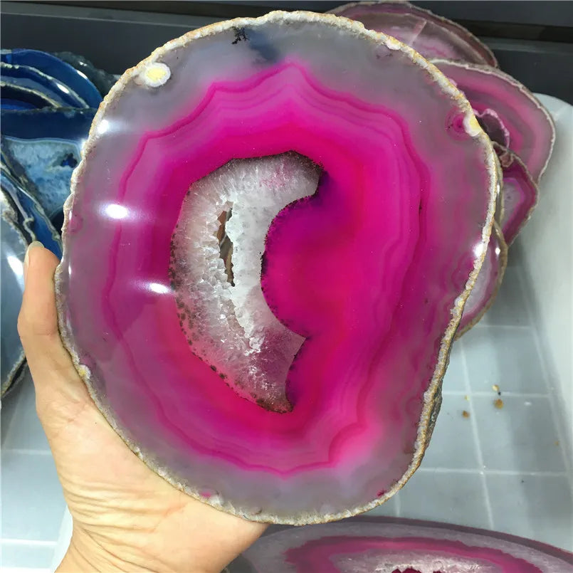 Hand holding a vibrant pink and gray agate slice with a blurred background