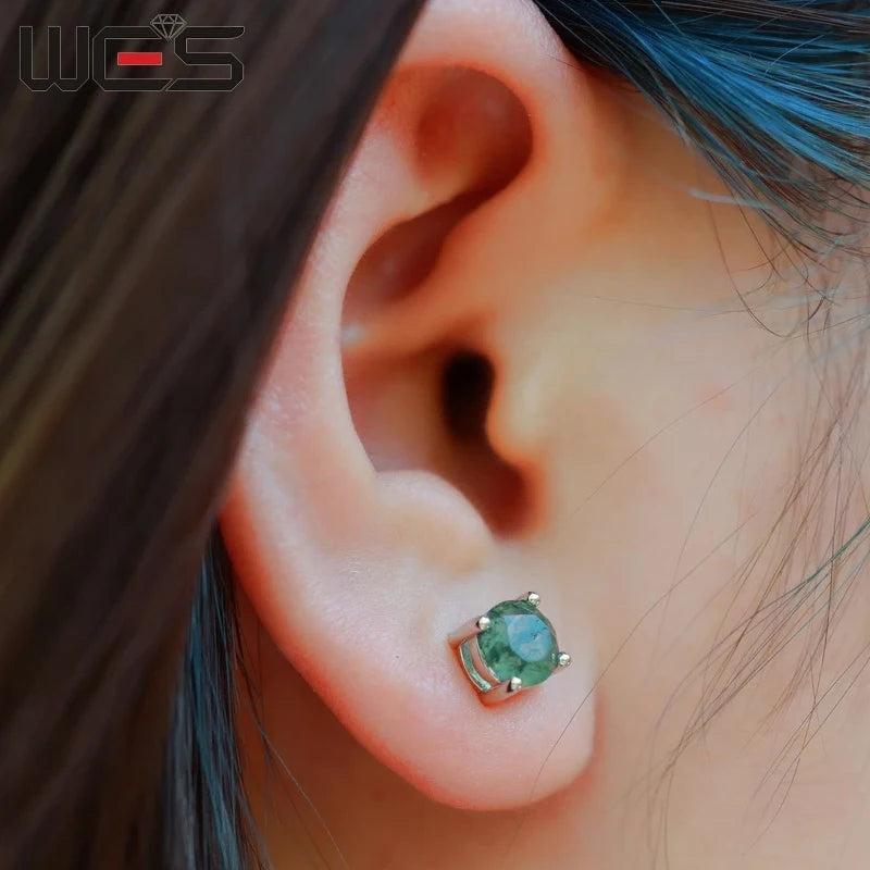 Close-up of an ear wearing a green gemstone earring with blurred hair in the background