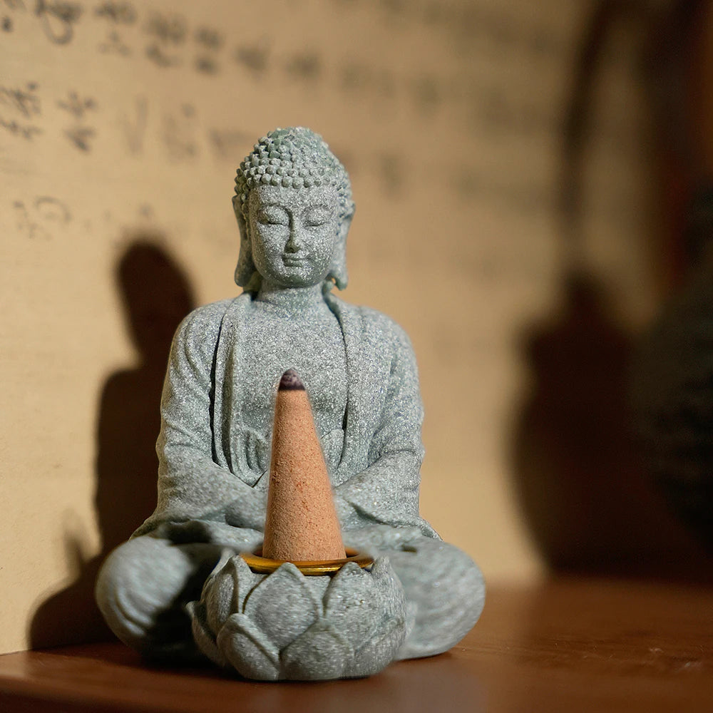 Stone Buddha statue with a incense cone holder on a wooden surface.