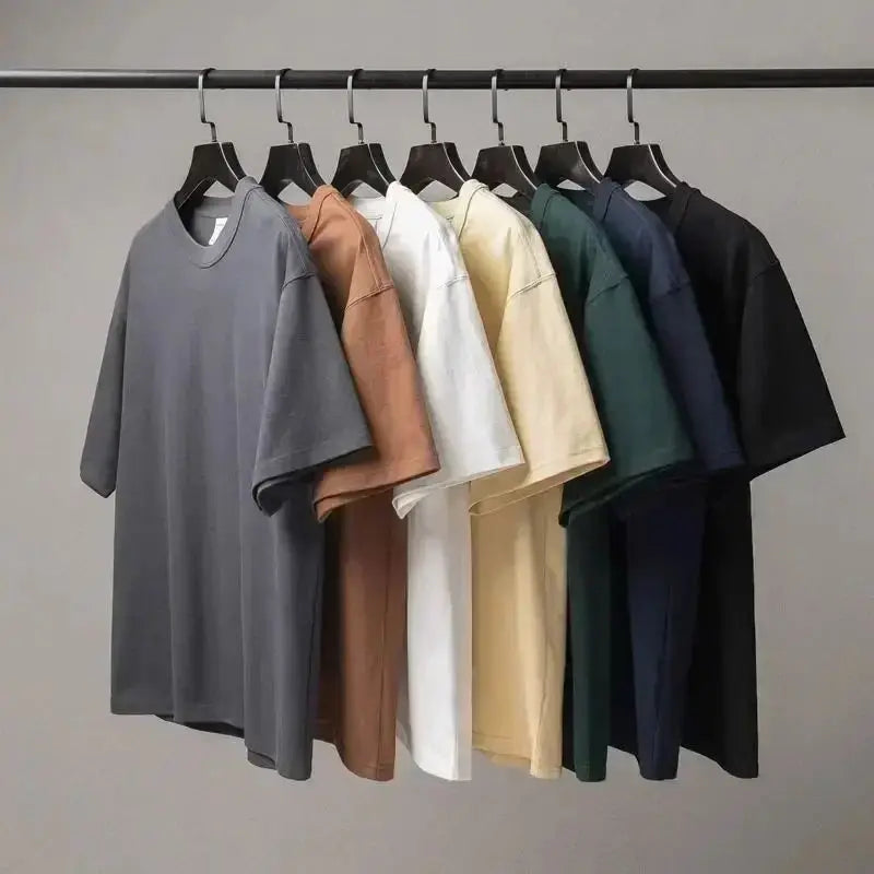 Set of five different colored shirts on hangers against a plain background